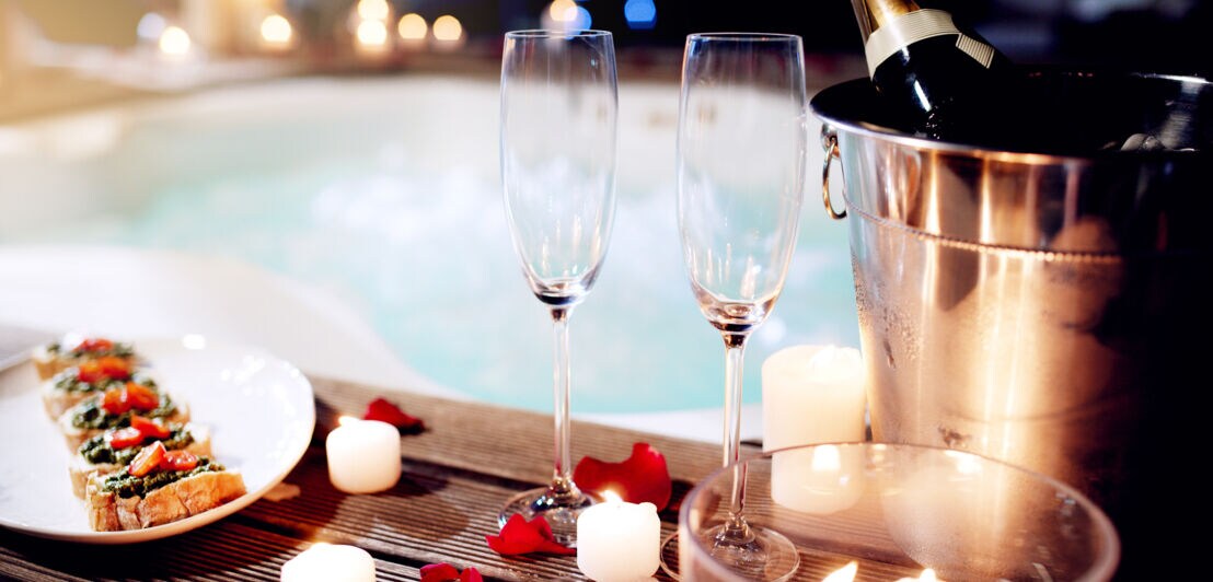 Romantisches Setting mit Sektgläsern, Kerzen und Bruschetta am Rand eines Whirlpools