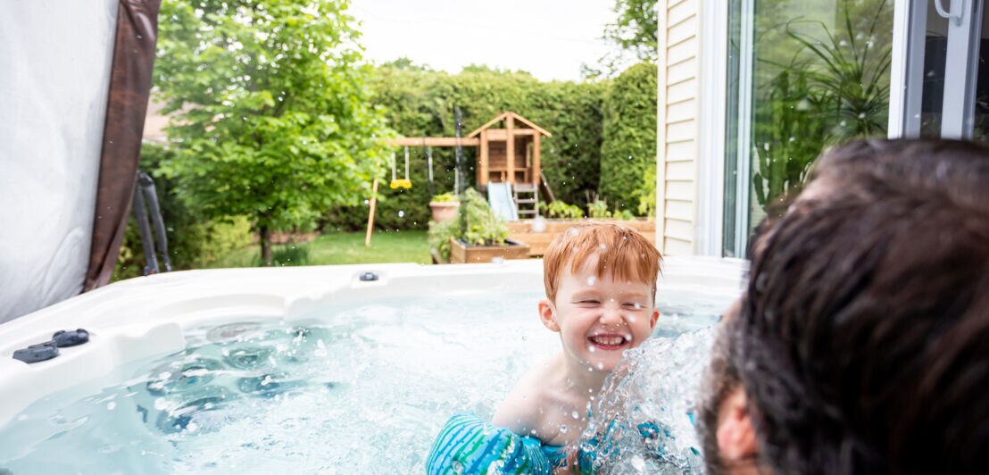 Ein kleiner rothaariger Junge hat mit seinem Vater Spaß im Whirlpool im Garten