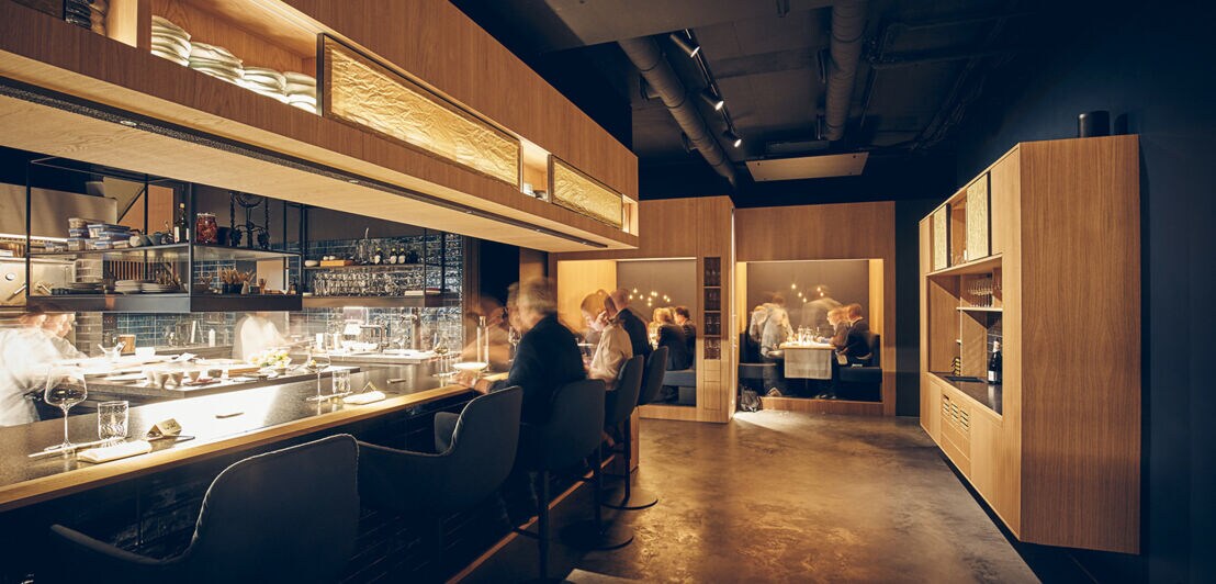 Blick in den Gastraum des Restaurants Intense mit langem Tresen und Sitznischen in einem Mix aus Industrie-Chic und warmen Hölzern.