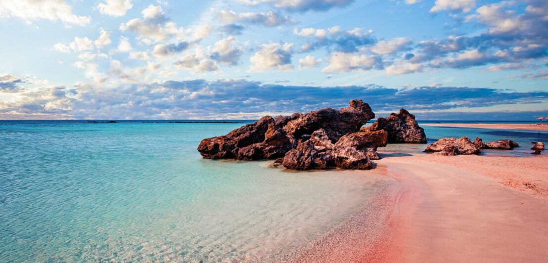 Ein Strand mit rosa Sand und Felsen im türkisblauen Wasser.