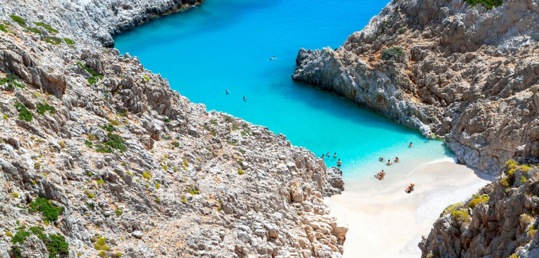 Aufsicht auf einen Sandstrand in einer felsigen Bucht mit türkisblauem Wasser.