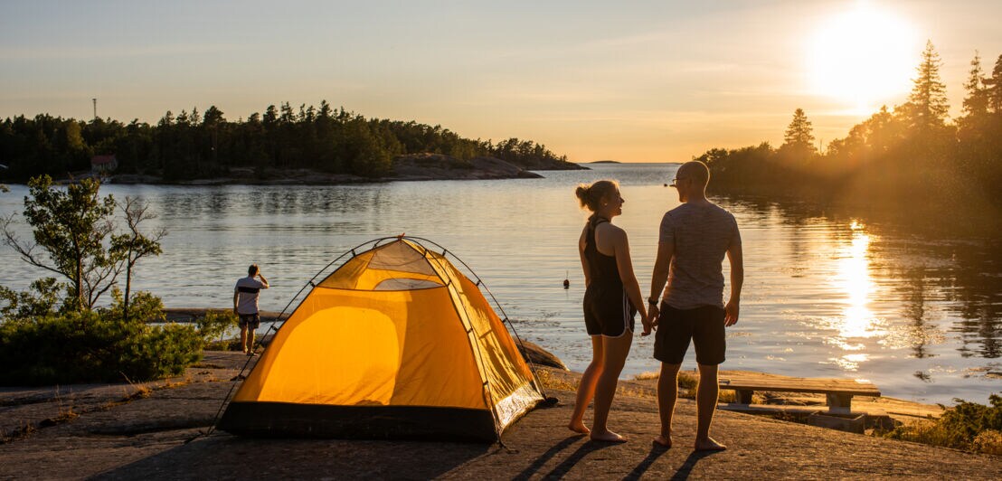 Drei Personen und ein Zelt an einem Gewässer in der Abendsonne