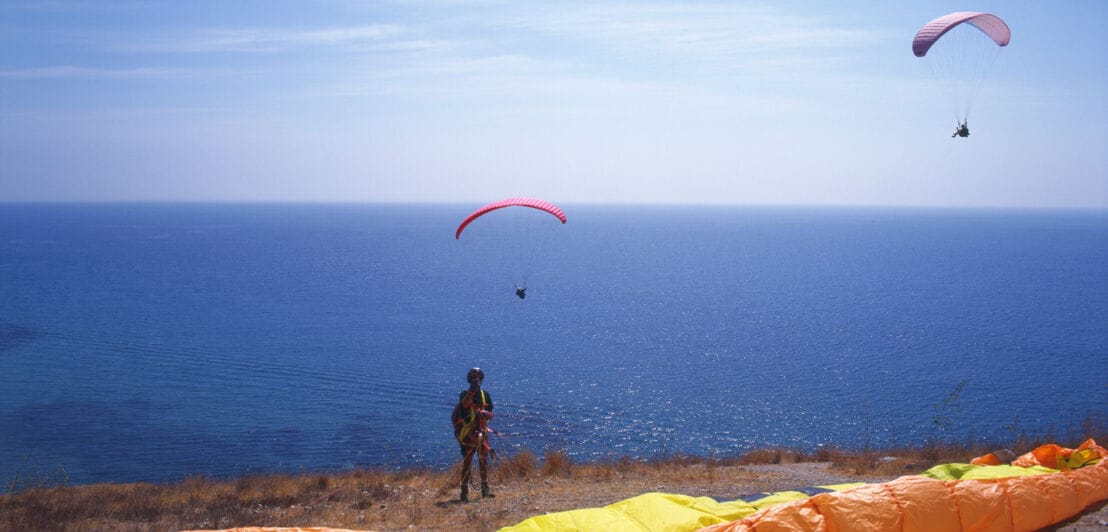 Ein Paraglider macht sich zum Absprung bereit, vor ihm das Meer