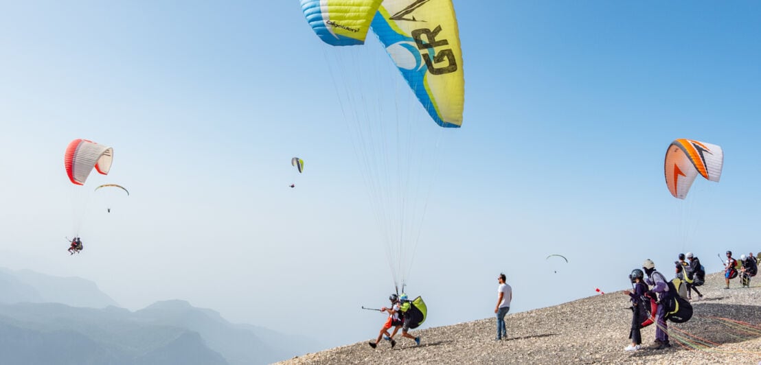 Mehrere Paraglider üben an einem Bergabhang den Absprung 