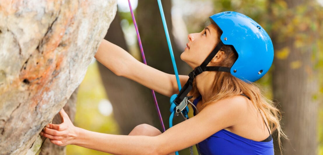 Ein Mädchen mit blauem Helm, das an einer Felswand klettert