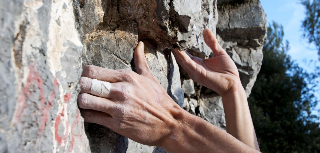 Die Hände eines Kletternden halten sich an einer Steinwand fest