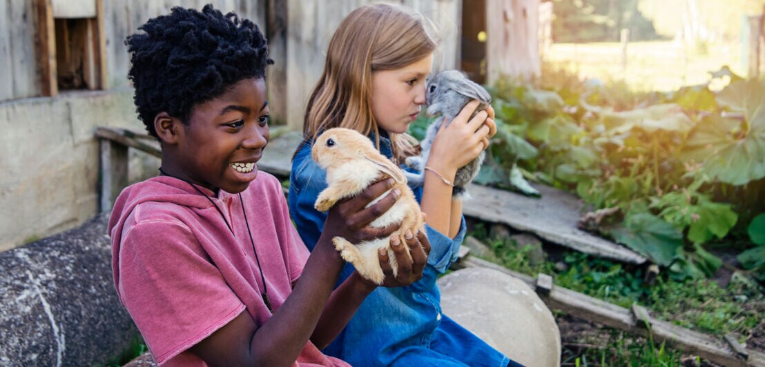 Zwei fröhliche Kinder halten jeweils ein kleines Kaninchen in den Händen