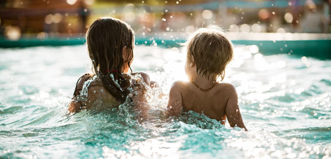 Zwei Kinder planschen im Schwimmbadbecken