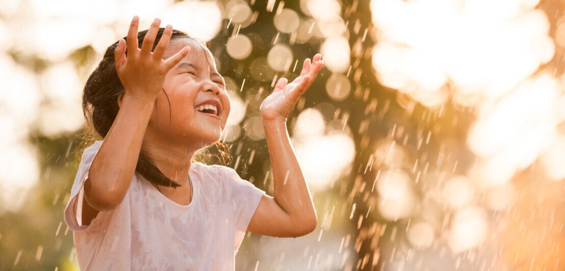 Ein kleines Mädchen wird von vielen Wassertropfen getroffen und freut sich