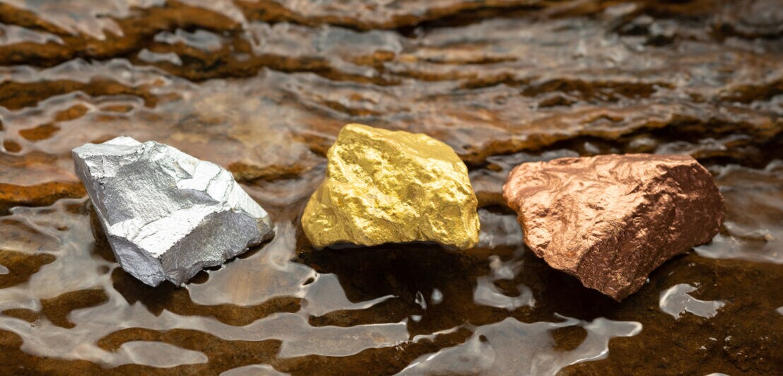 Mittelgroße Brocken aus reinem Gold, Silber und Kupfer auf felsigem Grund mit fließendem Wasser