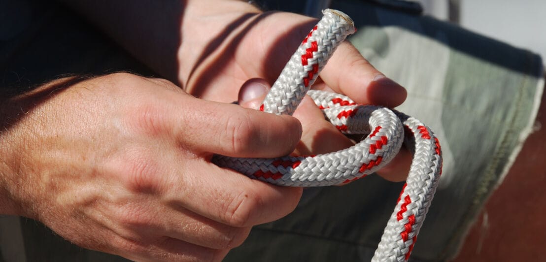 Zwei Hände, die ein weiß-rotes Seil zum Knoten schnüren