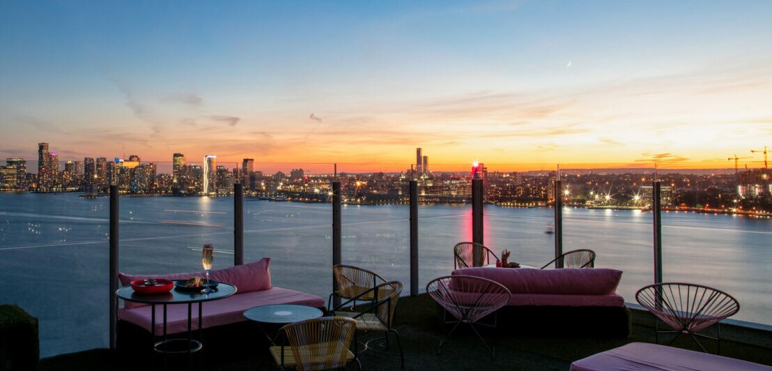 Eine Terrasse mit Polstermöbeln vor der Skyline New Yorks bei Sonnenuntergang