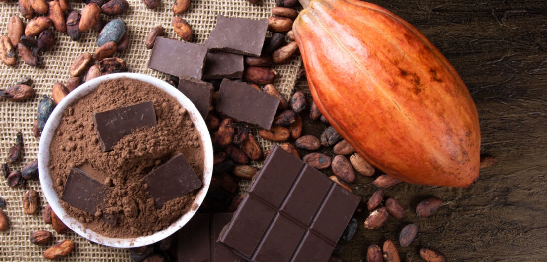 Kakaobohnen, Kakaopulver und Kakaostückchen auf einem Jutesack arrangiert