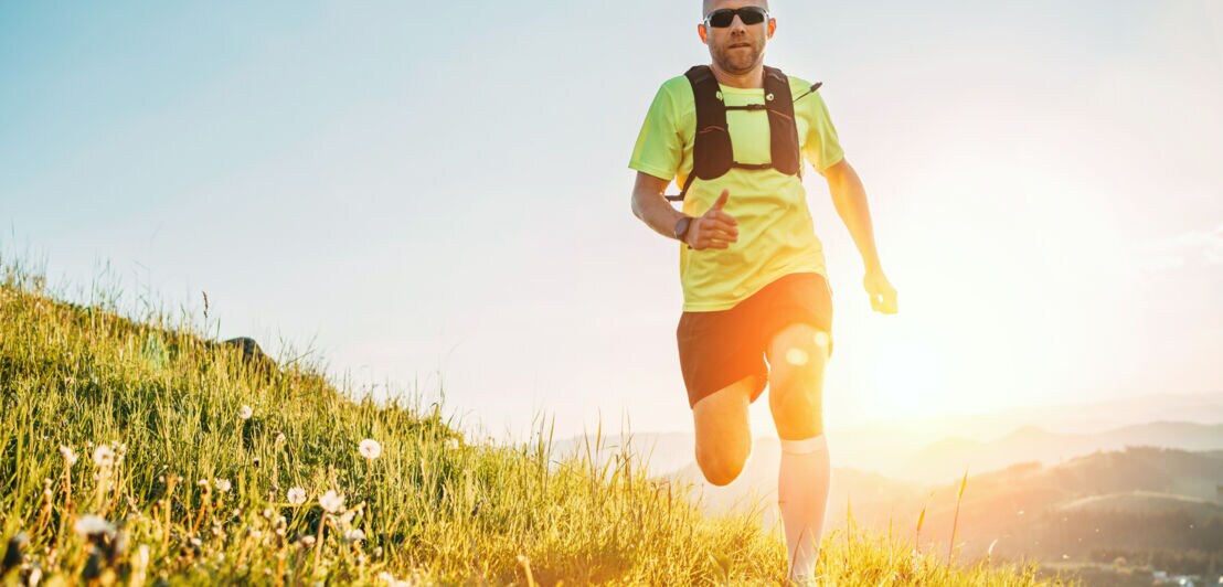 Ein Mann rennt in hügeligem Gelände auf die Kamera zu mit Sonne im Hintergrund