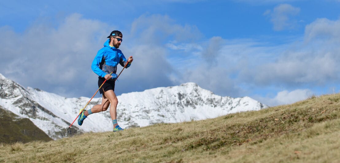Ein Mann rennt bei bestem Wetter in einem bergigen Gebiet und nutzt dabei Laufstöcker