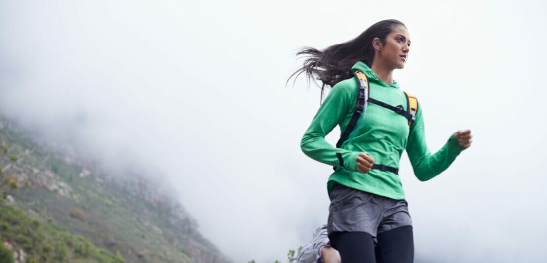 Eine Frau rennt bei nebeligem Wetter durch bergiges Gebiet