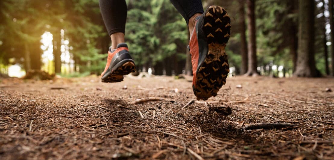 Detailaufnahme der Füße und Beine einer Person, die über einen Waldboden rennt