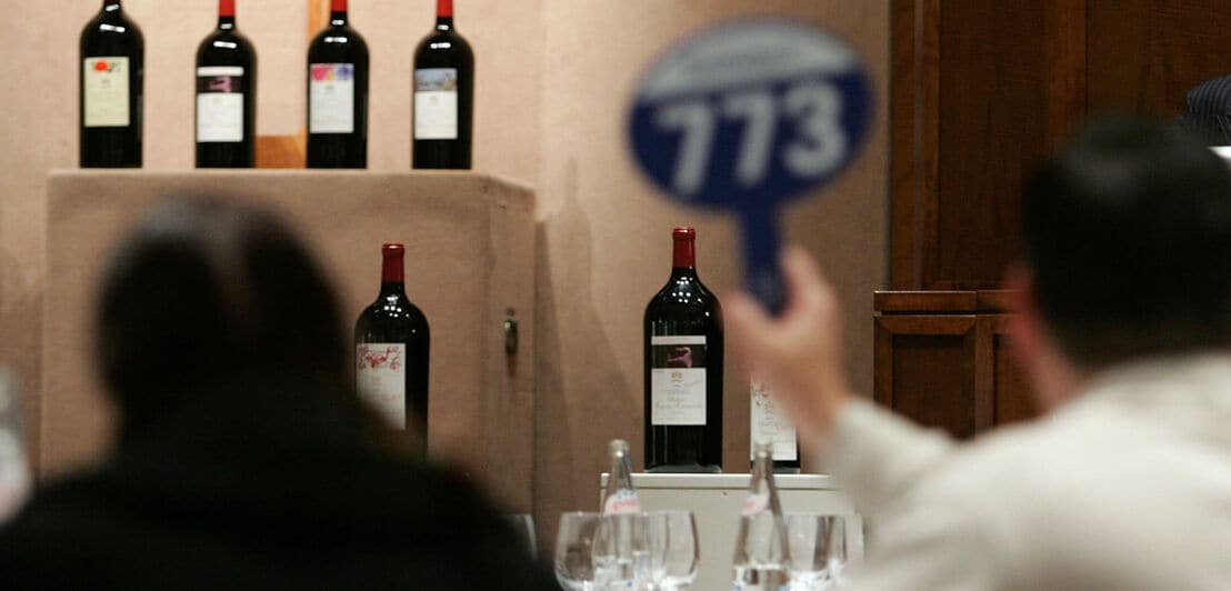 Käufer bei einer Auktion bieten mit Nummernschildern auf Rotweinflaschen der Marke Chateau Mouton Rothschild