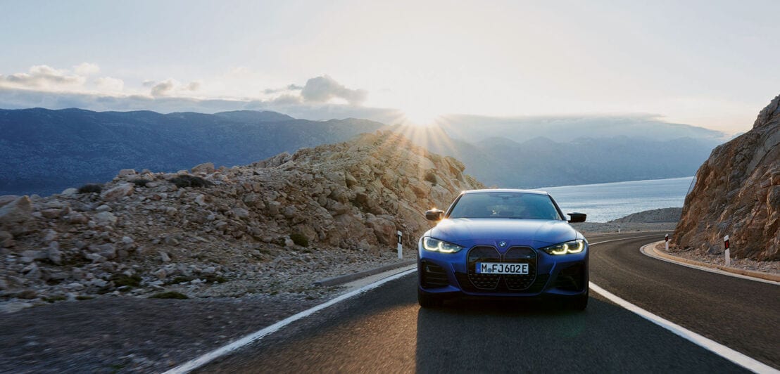Vorderansicht eines blauen Autos der Marke BMW, das auf einer gebirgigen Küstenstraße fährt