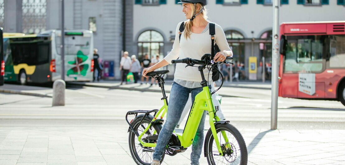 Eine junge Frau mit einem Klapp-E-Bike an einer Bushaltestelle