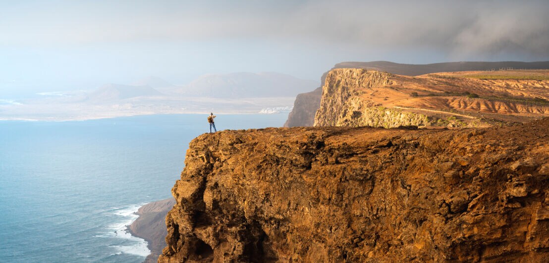 Küstenpanorama mit steiler Felsklippe, auf der eine Person steht