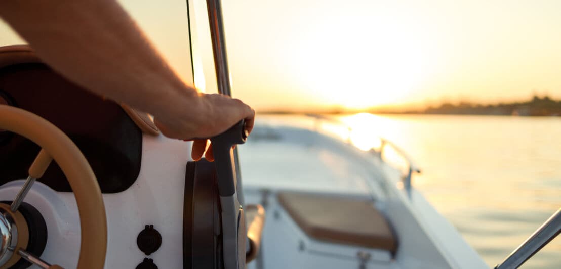 Nahaufnahme der Hand eines Mannes am Steuer eines Schnellboots bei Sonnenuntergang.