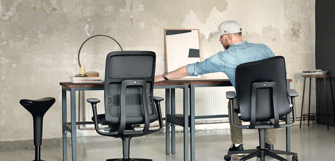 Rückansicht eines Mannes an einem Schreibtisch auf einem Schreibtischstuhl mit beweglicher Sitzfläche