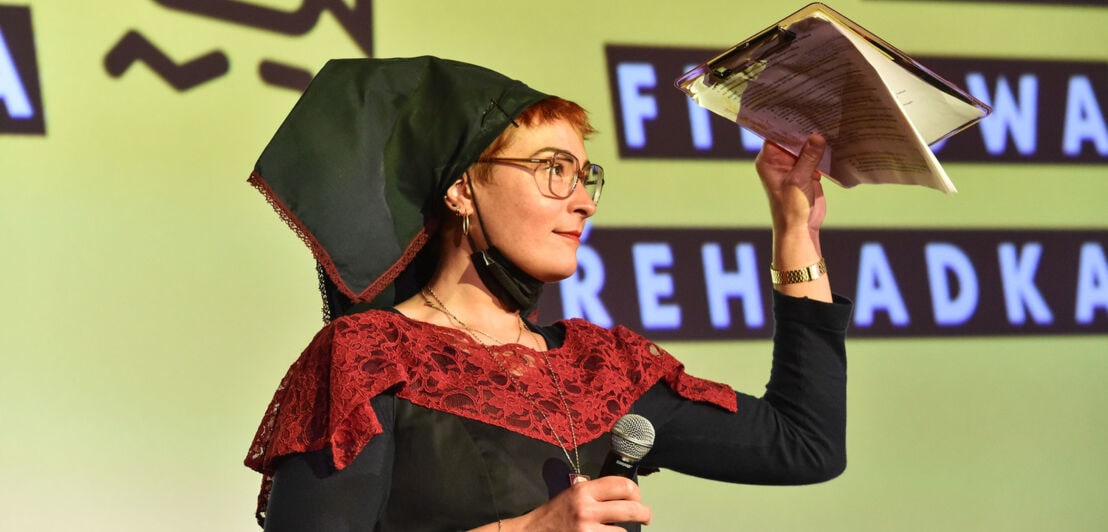Eine junge Frau in sorbischer Tracht auf einer Bühne mit Mikrofon beim Filmfestival Cottbus