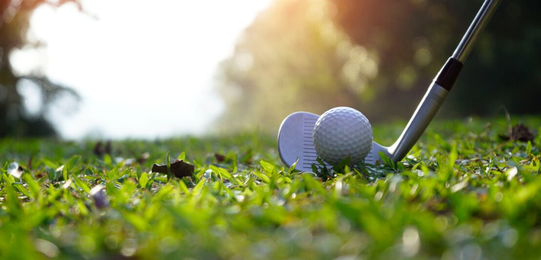Golfschläger am Golfball zum Abschlag auf grünem Rasen