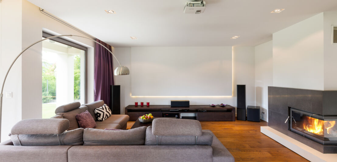 Ein modernes, großräumiges Wohnzimmer mit einer großen Leinwand und einem Beamer an der Decke