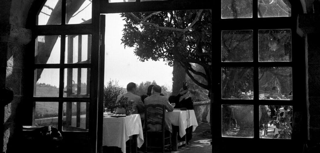 Historische Schwarzweiß-Fotografie des Restaurants La Colombe d’Or mit Gästen an einem Tisch auf der Terrasse (1949)
