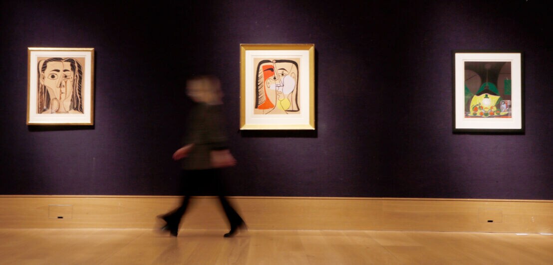 Eine Person geht in einem Ausstellungsraum an einer Wand mit drei Linolschnitten von Picasso vorbei