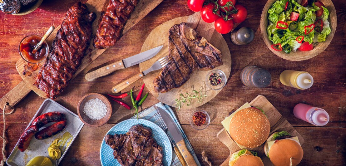 Aufsicht eines Holztisches mit gegrillten BBQ Variationen mit Steaks, Spareribs und Burgern