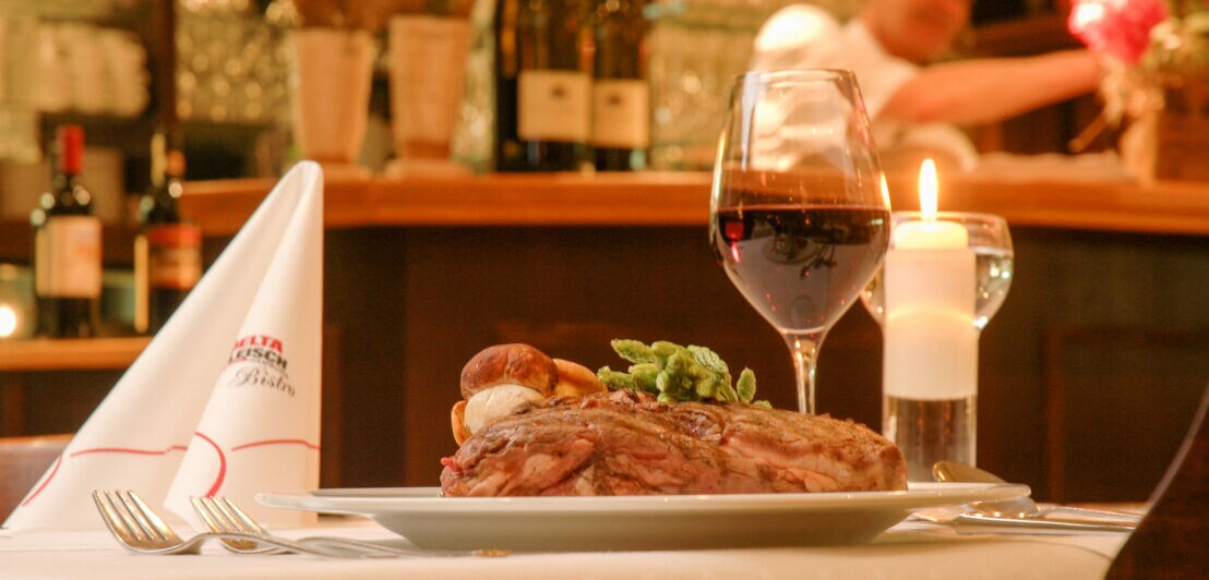 Ein gedeckter Restauranttisch mit Rotwein im Glas und Fleischgericht auf dem Teller.