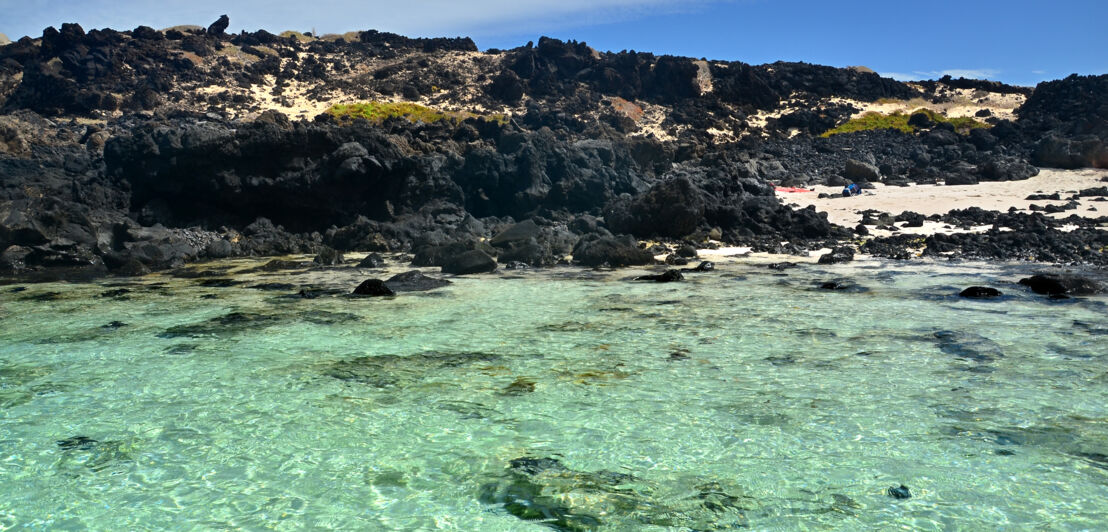 Blick auf den Strand von Caleton Blanco mit schwarzen Felsen und klarem Wasser