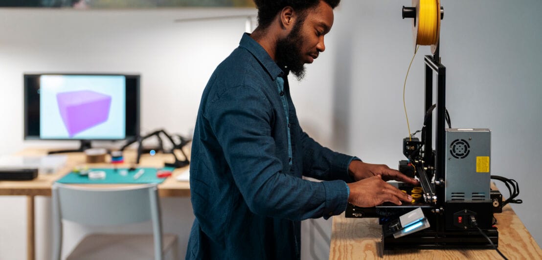 Profilansicht eines Mannes, der in einem häuslichen Arbeitszimmer einen 3D-Drucker bedient