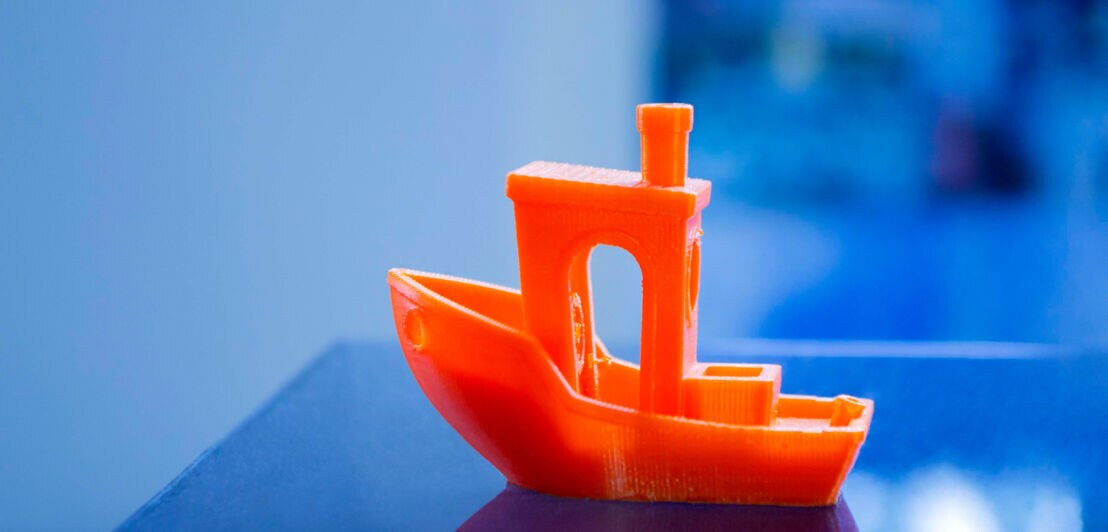 Ein kleines, mit einem 3D-Drucker erstelltes Modellboot aus orangenem Plastik 