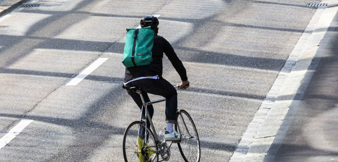 Ein Radfahrer fährt auf der Straße und trägt dabei einen Rucksack von FREITAG. 