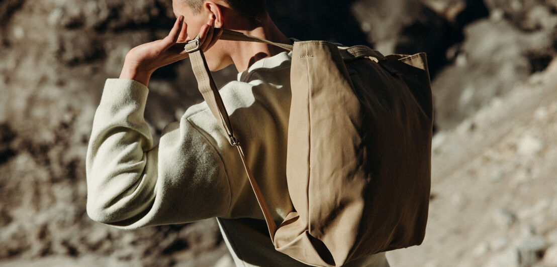 Ein männliches Model trägt in steiniger Umgebung einen Rucksack. 