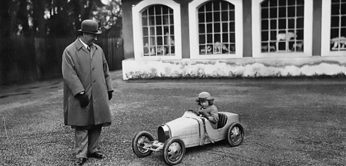 Schwarz-weiß-Aufnahme von einem Vater mit seinem Sohn, der in einem kleinen Automodell sitzt.