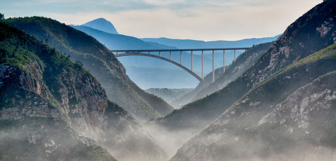 Blick vom Wasser auf eine Brücke, die zwei Berge miteinander verbindet