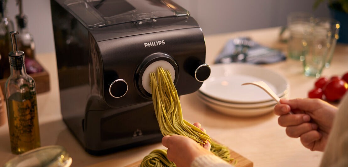 Eine Person fängt selbstgemachte Pasta aus einem Pastamaker auf