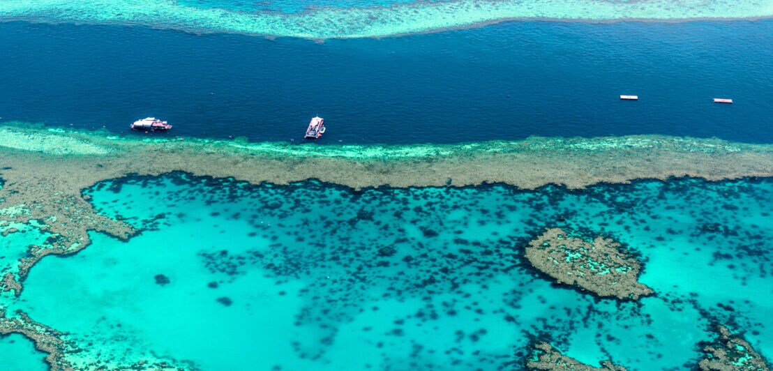 Türkisblaue Wasseroberfläche des Great Barrier Reef mit Booten aus der Luft