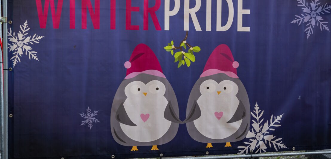 Zaunbanner mit der Aufschrift Winter Pride und einer Illustration zweier Pinguine, die Händchen halten