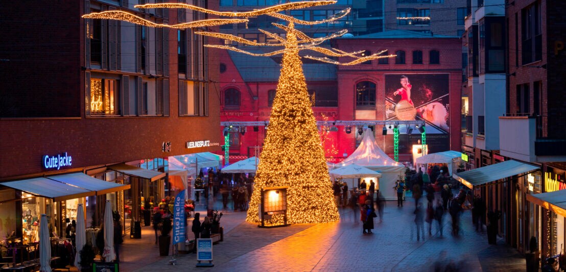 Erleuchteter Weihnachtsbaum mit Marktständen zwischen modernen Gebäuden in einer Einkaufsstraße