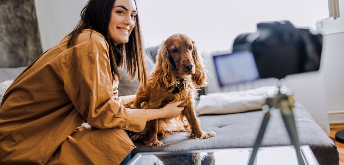 Eine junge Frau posiert mit Hund vor einer Kamera auf einem Stativ.