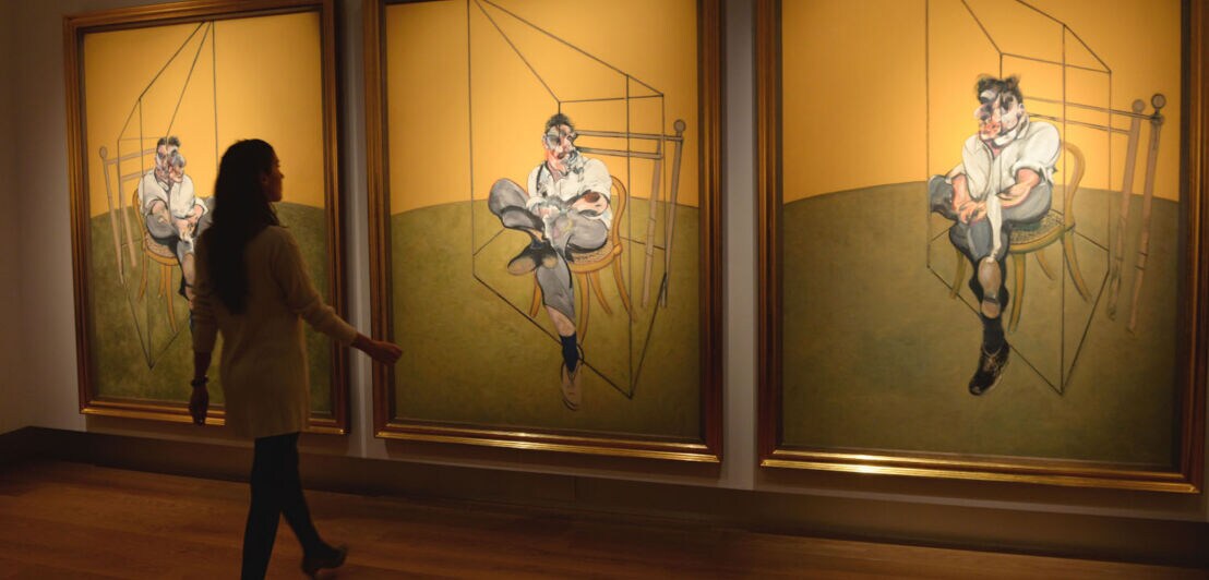 Eine Frau betrachtet drei Bilder von Francis Bacon in einem Museum