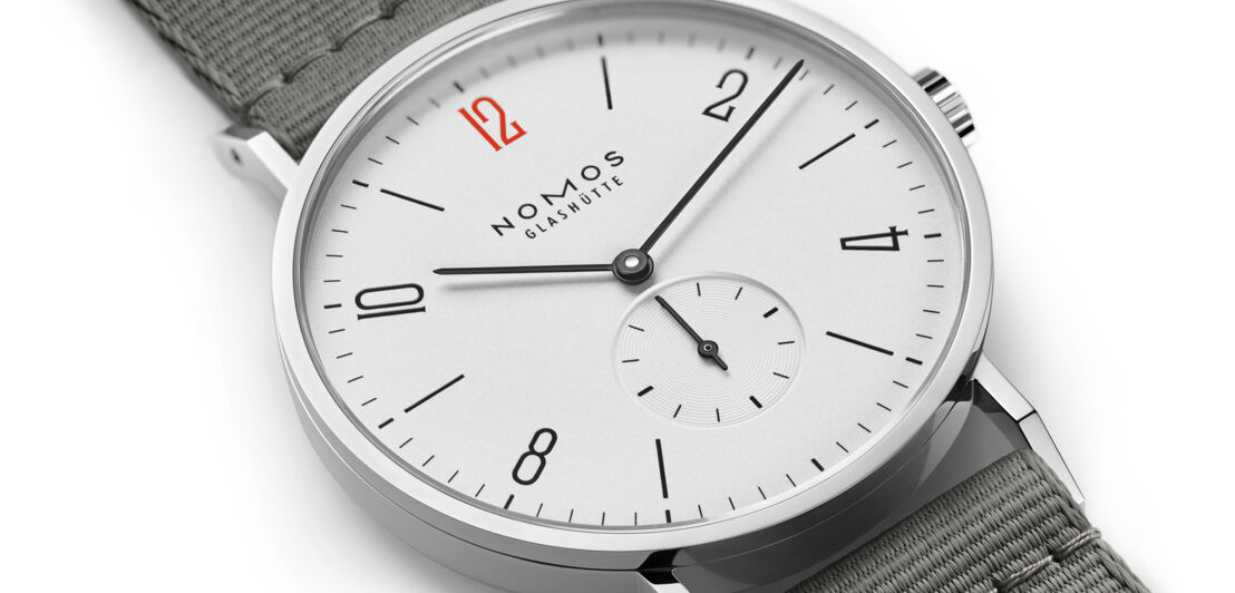 Silberne Armbanduhr mit weißem Zifferblatt, schwarzen Ziffern, grauem Armband und dem Schriftzug Nomos Glashütte.