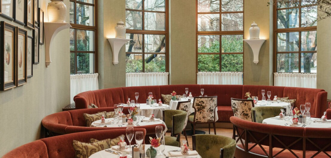 Schick gedeckte runde Tische am Fenster vor farbigen runden Polsterbänken in mediterranem Ambiente.