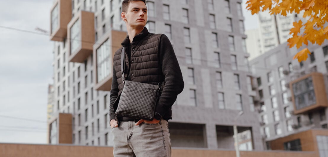 Fashion man holding black messenger bag in the autumn city